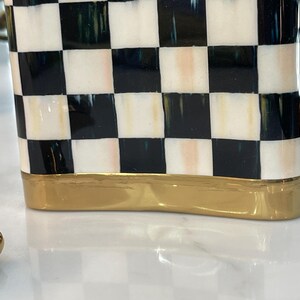 May include: A decorative ceramic container with a black and white checkered pattern. The base of the container is a gold color. The container is rectangular and has a smooth, glossy finish.