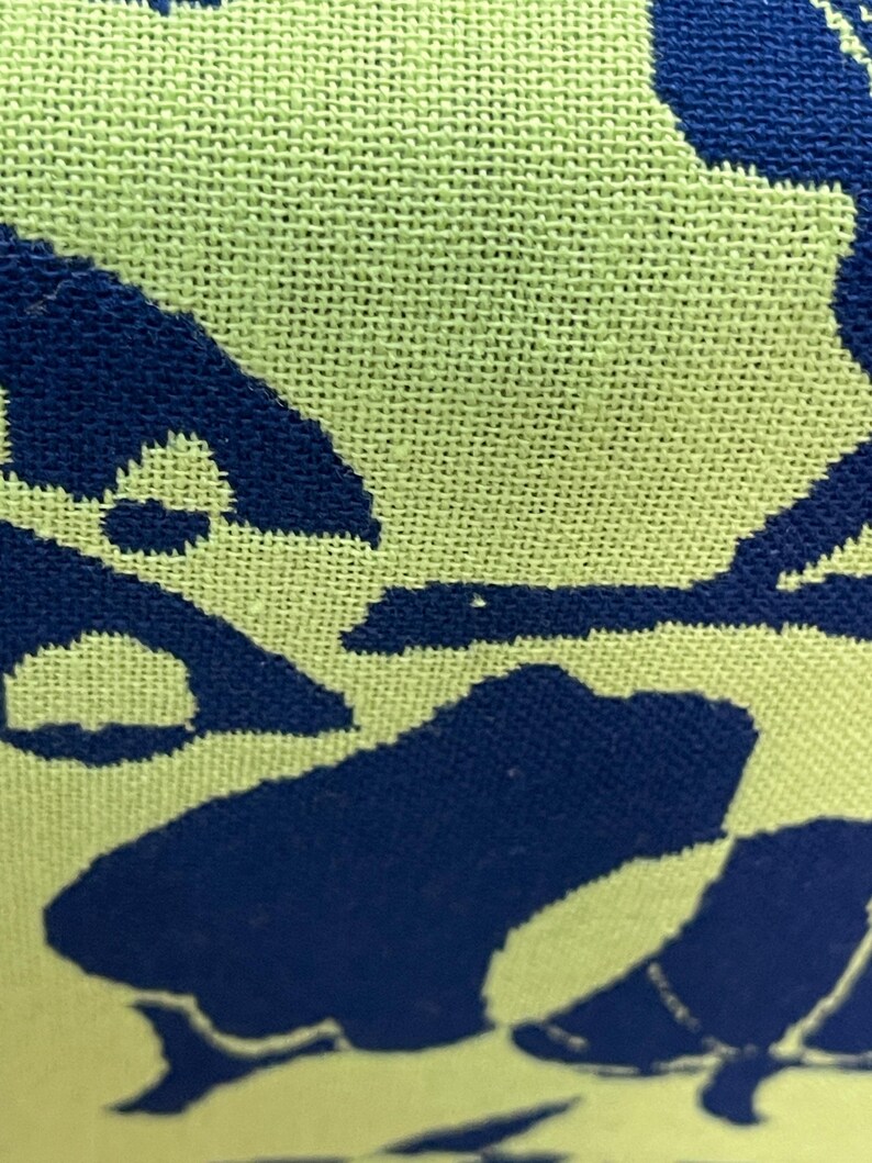 May include: Close-up of a woven fabric with a light green background and a dark blue pattern. The pattern appears to be a stylized floral or abstract design, with the blue shapes contrasting against the green.