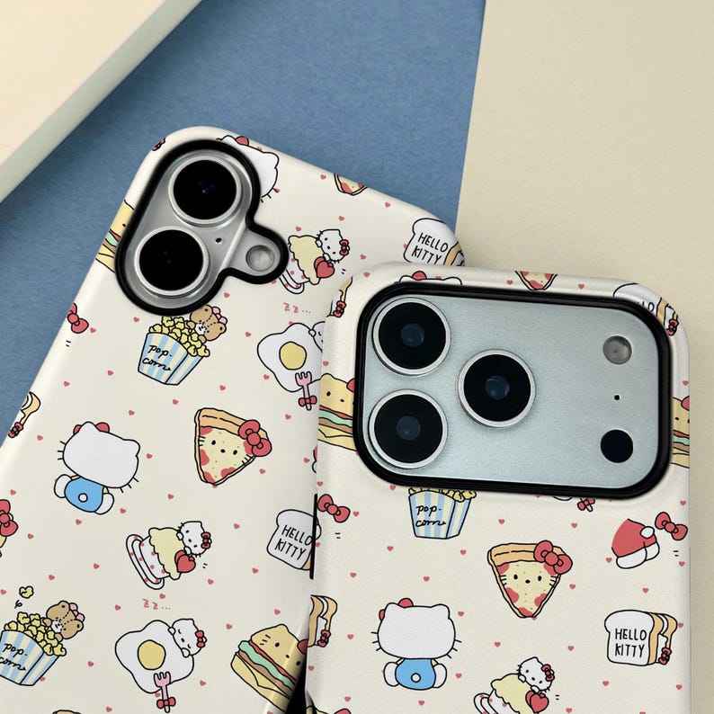 May include: Two phone cases with a cream background and a repeating pattern of Hello Kitty characters, popcorn, pizza, and eggs. The cases have black camera cutouts and the words "Hello Kitty" are printed on the cases.
