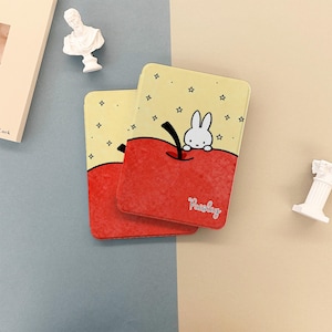 Op de afbeelding: Twee rechthoekige decoratieve items met een cartoon appel ontwerp. Een wit konijn kijkt over de rode appel. De achtergrond is geel met kleine zwarte sterren. Het woord "Parsley" is cursief geschreven op het rode gedeelte.