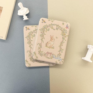 May include: Two rectangular, light pink cases with a floral and bunny design. The cases have a decorative border of green leaves and small birds. The word "Paisley" is written in cursive on the bottom right corner.