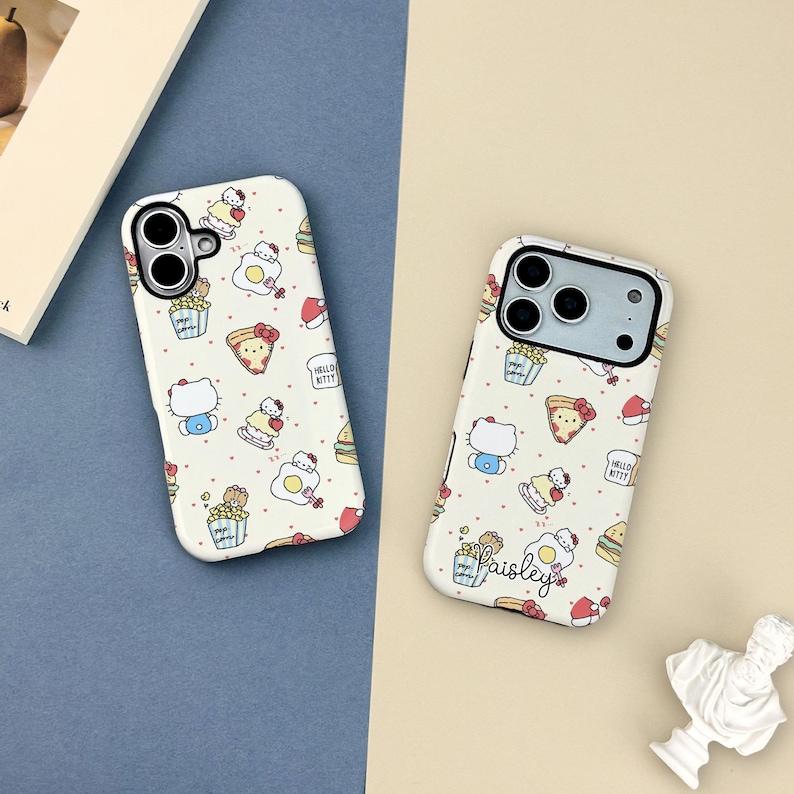 May include: Two white phone cases with a repeating pattern of cartoon characters, food items, and text. The cases feature a variety of illustrations, including Hello Kitty, popcorn, pizza, and eggs. One case has the name "Paisley" printed on it.