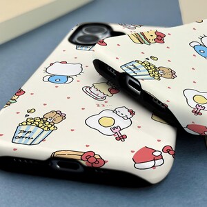 May include: Two white phone cases with a repeating pattern of cartoon characters, food items, and small red hearts. The cases have a black border and are likely for a smartphone. The design includes images of a cat, popcorn, and a fried egg.
