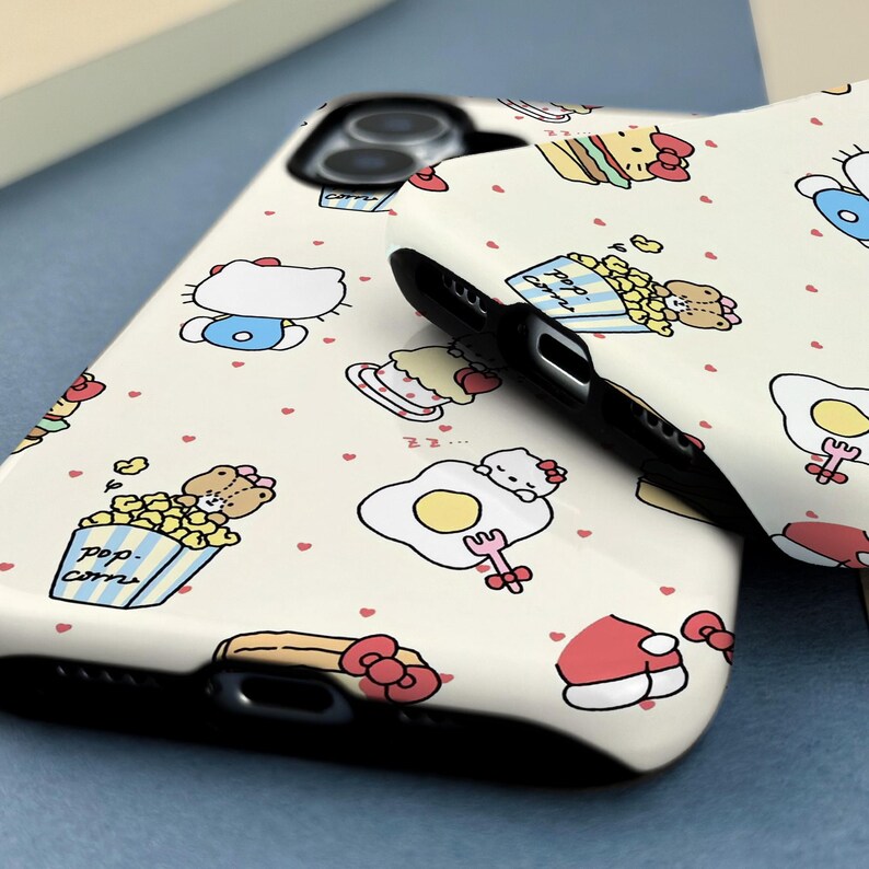 May include: Two white phone cases with a repeating pattern of cartoon characters, food items, and small red hearts. The cases have a black border and are likely for a smartphone. The design includes images of a cat, popcorn, and a fried egg.