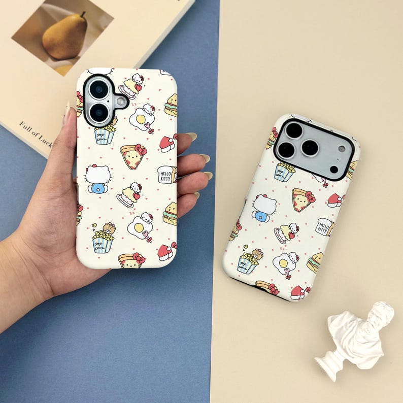 May include: Two white phone cases with a repeating pattern of Hello Kitty characters, food items, and the text "Hello Kitty". The cases are on a light background.