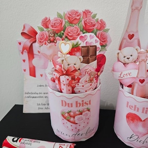 K&ouml;nnte beinhalten: Geschenkset zum Valentinstag mit rosa und roten Akzenten. Enth&auml;lt einen Papierstrau&szlig; Rosen, Teddyb&auml;ren, Geschenkboxen und herzf&ouml;rmige Dekorationen. Das Set enth&auml;lt einen Beh&auml;lter mit den Worten "Du bist wunderbar".