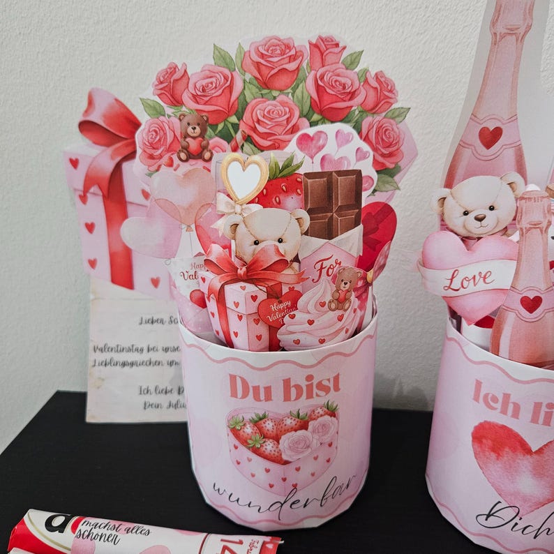 K&ouml;nnte beinhalten: Geschenkset zum Valentinstag mit rosa und roten Akzenten. Enth&auml;lt einen Papierstrau&szlig; Rosen, Teddyb&auml;ren, Geschenkboxen und herzf&ouml;rmige Dekorationen. Das Set enth&auml;lt einen Beh&auml;lter mit den Worten "Du bist wunderbar".