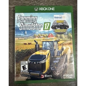 May include: A physical Xbox One game case for Farming Simulator 17. The cover art features a yellow tractor in a field of sunflowers with mountains in the background. It includes an ESRB E rating and a circular sticker for bonus content.