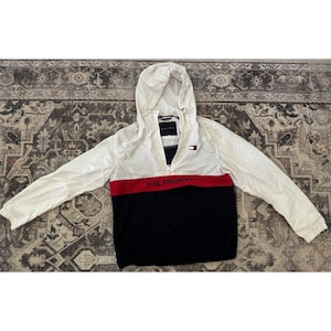 May include: White, red, and black hooded jacket with a zipper closure. The jacket features a red band across the chest with the word "HILFIGER" in white letters. A small logo is visible on the chest.