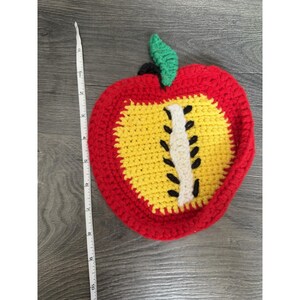 Puede incluir: Un salvamanteles hecho a mano en forma de manzana de ganchillo. El salvamanteles presenta un exterior rojo, un interior amarillo y una hoja verde. La manzana mide aproximadamente 20 cm de largo.