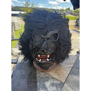 以下が含まれることがあります： 黒い狼男のマスク。マスクは、牙が見え、頭の周りに毛皮のような質感を持つ詳細な顔を特徴としています。目は暗く空洞で、マスクの不気味さを増しています。ハロウィーンのコスチュームアクセサリー。
