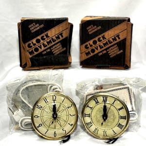 May include: Two clock movements with gold-colored rims and cream-colored faces. One has Arabic numerals, the other Roman numerals. The image also shows two boxes labeled "CLOCK MOVEMENT" and the text "HERE'S ANOTHER GUARANTEED".