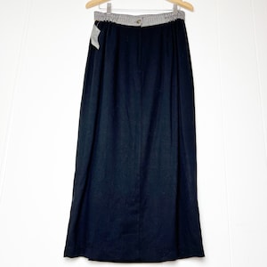 May include: A black maxi skirt with a white and black striped waistband. The skirt has a straight silhouette and a simple design.