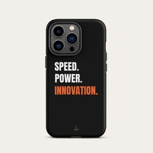 Può includere: Custodia per telefono nera con le parole "SPEED. POWER. INNOVATION." in lettere bianche e arancioni. La custodia ha una finitura lucida e un ritaglio per la fotocamera nella parte superiore. In basso c'è una piccola firma.
