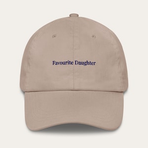 Könnte beinhalten: Beige Baseball Cap mit dem navyblauen Text "Favourite Daughter". Die Kappe hat einen gebogenen Schirm und einen verstellbaren Riemen auf der Rückseite. Hergestellt aus einem weichen, strapazierfähigen Material.