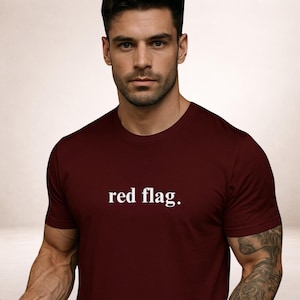 Könnte beinhalten: Ein weinrotes T-Shirt mit Rundhalsausschnitt und dem weißen Schriftzug "red flag." mittig auf der Brust. Das kurzärmelige Shirt scheint aus einem weichen Material zu sein.