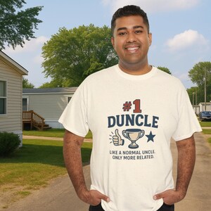 May include: A cream-colored t-shirt with the text "#1 DUNCLE" in navy blue and red, along with a thumbs-up, trophy, and star graphic. The text below reads, "LIKE A NORMAL UNCLE, ONLY MORE RELATED."