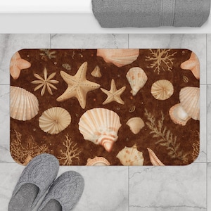 May include: A rectangular bath mat featuring a brown background with a pattern of seashells, starfish, and coral in shades of beige and tan. The mat is placed on a tiled floor, with a pair of gray slippers visible in the foreground.
