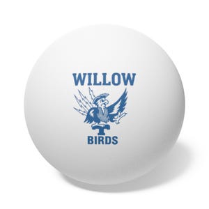May include: A white ping pong ball with a blue logo featuring a bird wearing a tricorn hat, wings spread, and lightning bolts. The text "WILLOW BIRDS" is above and below the bird.