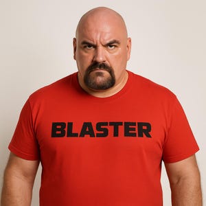 May include: A bald man with a goatee wearing a red t-shirt with the word "BLASTER" printed in large, black letters. The man has a stern expression and is looking directly at the camera.