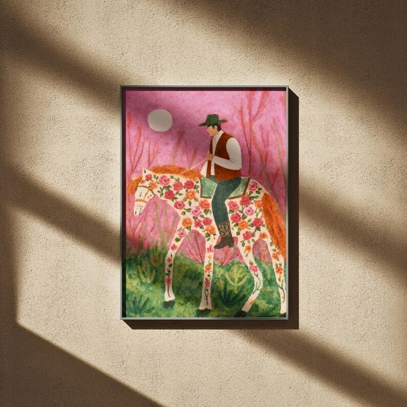 Op de afbeelding: Een ingelijste illustratie toont een persoon op een paard versierd met bloemmotieven. De ruiter draagt een groene hoed en vest. De achtergrond toont een roze landschap met een volle maan, wat een grillige, artistieke sc&egrave;ne cre&euml;ert.