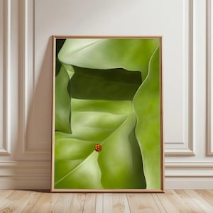 May include: A framed art print featuring a close-up of large, vibrant green leaves with a ladybug. The artwork is set in a natural wood frame, creating a striking contrast against the white wall and wooden floor.