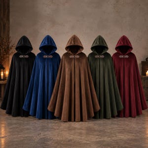 May include: Five floor-length hooded cloaks in black, blue, brown, dark green, and deep red. Each cloak features a smooth, solid-colored fabric, a pointed hood, and a decorative metal clasp closure at the neck with two small leather-like tabs.