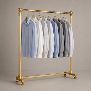 以下が含まれることがあります： ゴールドトーンの金属製衣類ラックで、水平バーとベースに4つの小さなキャスターが付いています。ラックには、青、白、グレー、ストライプ柄の長袖ボタンダウンシャツが8枚、ゴールドのハンガーに掛かっています。