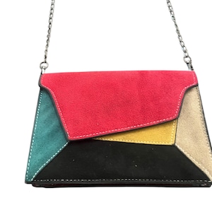May include: A geometric-patterned clutch with a silver chain strap. The bag features a patchwork design with red, teal, yellow, black, and tan suede-like panels. White stitching outlines the edges of the colorful sections.
