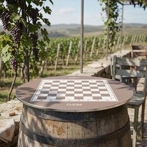 Peut inclure: Une table de jeu d'échecs ronde avec une surface marron et un échiquier à carreaux blancs et marron. La table est soutenue par un tonneau en bois. Le mot "CHESS" est imprimé sur la table. La table est à l'extérieur.