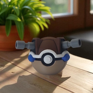 May include: A brown, white, and blue toy with two gray cylinders extending from the sides. The toy is spherical with a circular design in the center. The background includes a potted plant and a wooden surface.