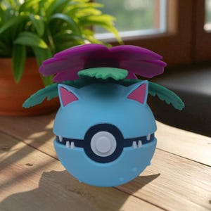 May include: A light blue, spherical figure with a purple flower and green leaves on top. The figure has a white and black circle in the center and white teeth. The figure is on a wooden surface.