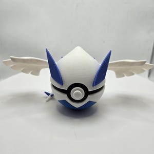 May include: A 3D-printed white, blue, and black figurine of a stylized creature with wings. The figure has a rounded body with blue accents and wings extending from the sides. The design resembles a popular character from a video game.