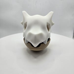 May include: A white skull-shaped figurine with pointed ears and a brown base. The figurine is a stylized representation of a skull, with detailed features and a smooth finish. The object is likely a collectible or decorative item.