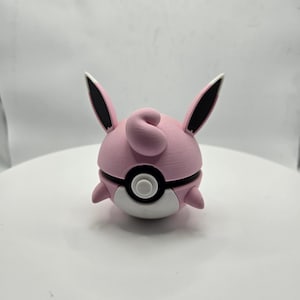 May include: A pink and white 3D-printed figure resembling a Jigglypuff-like character. The figure has large ears with black tips, a curled tuft of hair, and a round body with a black and white design. The figure is a collectible item.