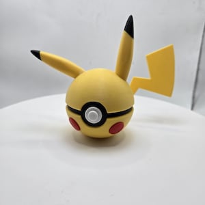 May include: A yellow and black Pikachu-themed ball with red accents. The ball has Pikachu's ears and a lightning bolt tail. The ball is a sphere with a black and white circle in the middle and red circles on the sides.
