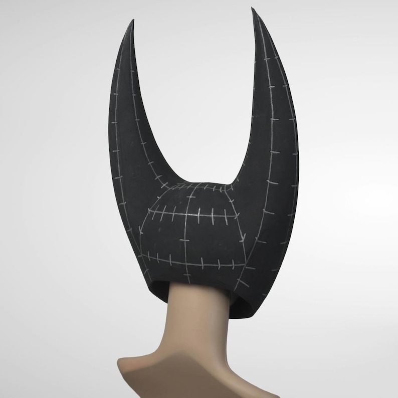 May include: A black horned headpiece with a curved design. The headpiece is worn on a mannequin head. The horns are long and pointed, with a textured surface. White stitching lines the surface of the headpiece.