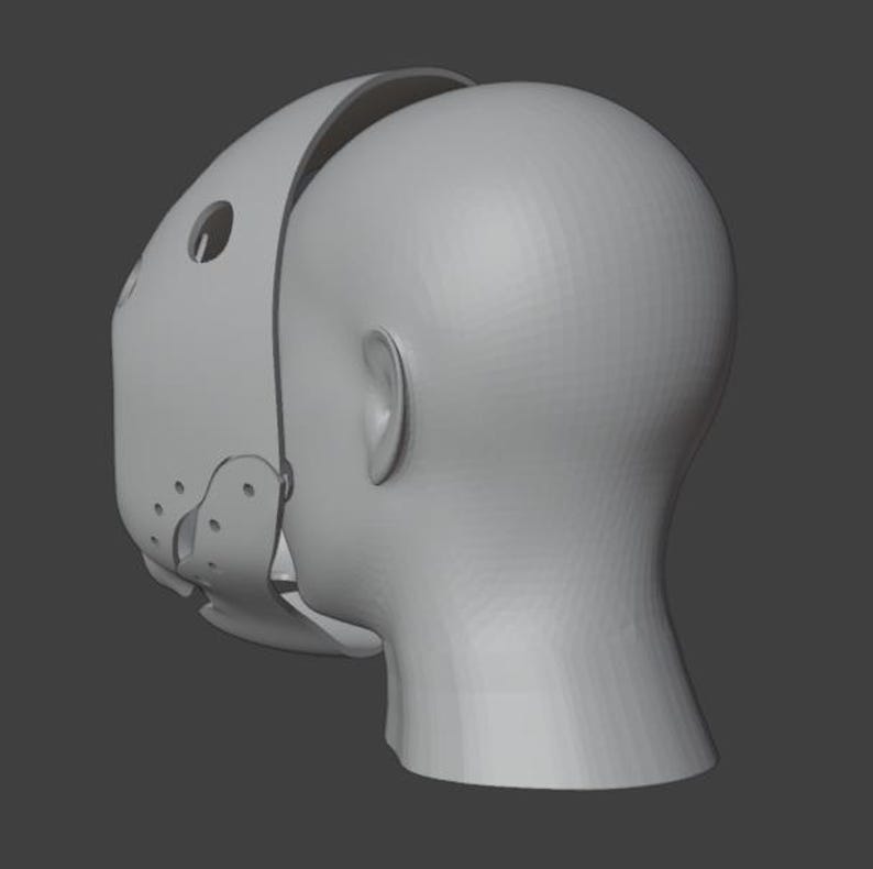 Op de afbeelding: Een lichtgrijze, 3D-geprinte muilkorfmasker met een gebogen ontwerp, met cirkelvormige en ovale openingen. Het masker is gedeeltelijk bevestigd aan een 3D-geprinte kop, met het oor en de nek.