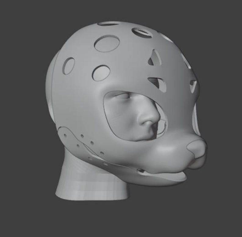 Op de afbeelding: Een grijze, 3D-gemodelleerde hoofdbedekking met een gestileerd dierengezichtontwerp. Het masker heeft meerdere cirkelvormige en ovale uitsparingen, met openingen voor de ogen en mond. Het ontwerp omvat een neus en een afgeronde snuit.