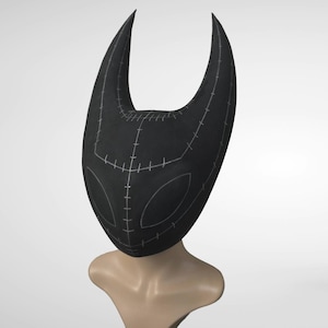 May include: A black mask with a horned design, featuring white stitching details. The mask has a stylized face shape with two eye openings. The mask is displayed on a mannequin head.