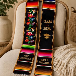 Puede incluir: Una estola de graduación negra con acentos de tela a rayas multicolores en los extremos y bordes. Un lado muestra patrones florales bordados y el texto 'FIRST GENERATION'. El otro lado presenta 'CLASS OF 2026', un icono de birrete dorado y el nombre 'EDITH MAGANA'.