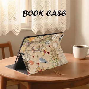 May include: A tablet case with a colorful Winnie the Pooh design, featuring characters and scenes from the Hundred Acre Wood. The case is open and propped up on a wooden table, with the words "BOOK CASE" printed at the top.