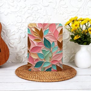 May include: A rectangular decorative panel with a floral design. The panel features stylized leaves in shades of pink, teal, brown, and gold against a light pink background. The panel is displayed on a round woven placemat.