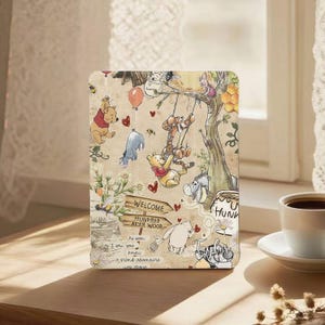 May include: A beige tablet case featuring a whimsical illustration of Winnie the Pooh and friends. The design includes a tree, honey pot, balloons, and the text "WELCOME HUNDRED AKER WOOD". The case has a vintage, storybook aesthetic.