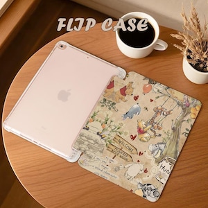 May include: A clear iPad flip case with a Winnie the Pooh design. The case features a tan background with illustrations of Pooh, Tigger, Eeyore, and Piglet. The text "FLIP CASE" is at the top. A cup of coffee and a small plant are also in the image.