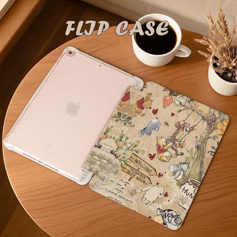 May include: A clear iPad flip case with a Winnie the Pooh design. The case features a tan background with illustrations of Pooh, Tigger, Eeyore, and Piglet. The text "FLIP CASE" is at the top. A cup of coffee and a small plant are also in the image.