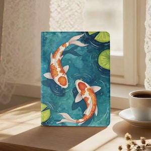 Puede incluir: Una funda rectangular para tableta con una ilustración en acuarela de dos peces koi naranjas y blancos nadando en agua azul profundo con nenúfares verdes. El diseño cubre toda la superficie frontal de la funda con trazos fluidos.