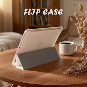 May include: A clear flip case for a tablet, propped up on a gray stand. The text "FLIP CASE" is displayed in a stylized font. A white mug of coffee sits on a wooden table, with dried flowers in the background.