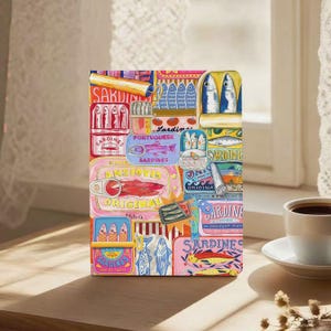 May include: A colorful, rectangular art print featuring various sardine can designs. The print showcases a collage of sardine cans with text like "Sardines" and "Portuguese Sardines" in a variety of colors and styles.