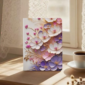 May include: A notebook with a floral design. The design features white, purple, and pink flowers with gold accents. The flowers are arranged in a layered pattern, creating a 3D effect. The notebook is on a wooden surface.